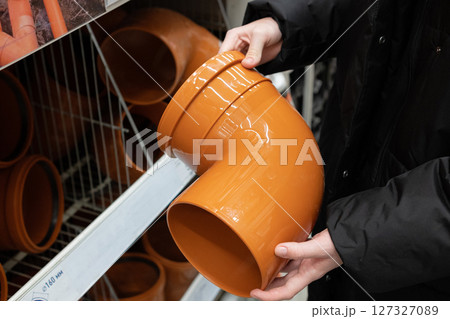 Person holding yellow PVC pipe fitting while shopping in home improvement store aisle during daytime 127327089