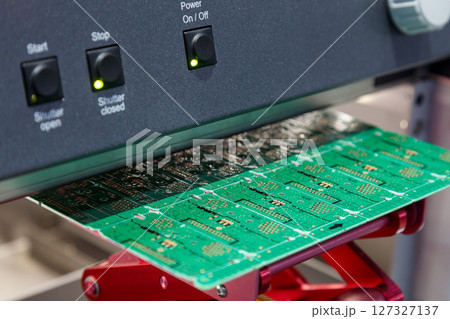 electronic circuit board under processing machine. Close-up of green PCB manufacturing stage with illuminated control panel. Electronic components production and assembly line. electronic circuit board under processing machine. Close-up of green PCB manufacturing stage with illuminated control panel. Electronic components production and assembly line. 127327137