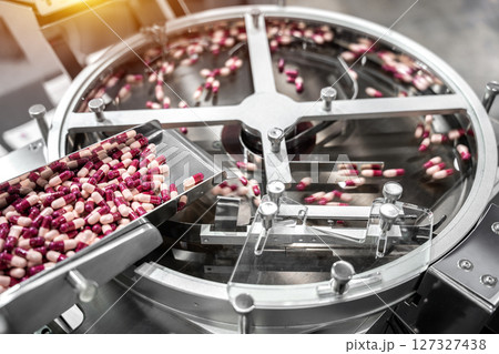 Pink and white capsules pills in the pills packaging machine, pharmacy medicine capsule pill in production line at medical factory. Pink and white capsules pills in the pills packaging machine, pharmacy medicine capsule pill in production line at medical factory. 127327438