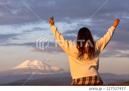 Woman Mountain Flowers: Girl raises flowers on hill during sunrise admiring peak landscape. Woman Mountain Flowers: Girl raises flowers on hill during sunrise admiring peak landscape. 127327457