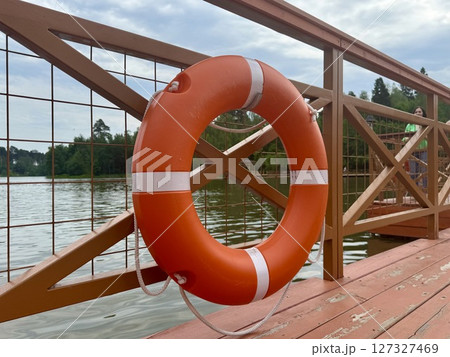 An orange and white lifebuoy hangs on a wooden bridge on a warm sunny day. High quality photo An orange and white lifebuoy hangs on a wooden bridge on a warm sunny day. High quality photo 127327469