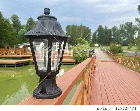 A black street lamp stands on a wooden bridge on a warm sunny day. High quality photo A black street lamp stands on a wooden bridge on a warm sunny day. High quality photo 127327471