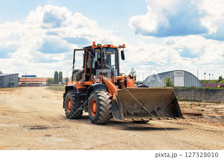 A large front loader transports crushed stone or gravel in a bucket at a construction site or concrete plant. Transportation of bulk materials. Construction equipment. Bulk cargo transportation. A large front loader transports crushed stone or gravel in a bucket at a construction site or concrete plant. Transportation of bulk materials. Construction equipment. Bulk cargo transportation. 127328010