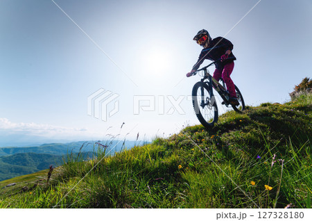 Mountain biker riding down a grassy slope. Enduro mountain bike. MTB against a mountain landscape 127328180
