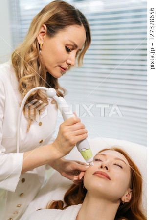 Process of skin rejuvenation procedure from of microneedling professional performing on female lying with closed eyes on treatment bed, targeting dermal renewal with precision handheld device 127328656