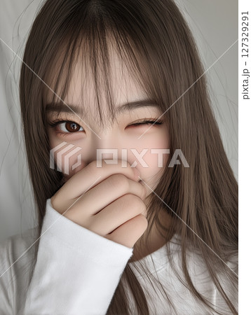 Young Korean woman smiling playfully while covering her mouth with her hand in a bright indoor setting 127329291