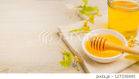 Honey bee in glass jar and bowl with linden flower with honey dipper on wooden background. 127330895