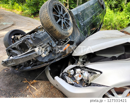 Silver sedan flipped over black vehicle are tangled after collision on quiet, wooded road. 127331421