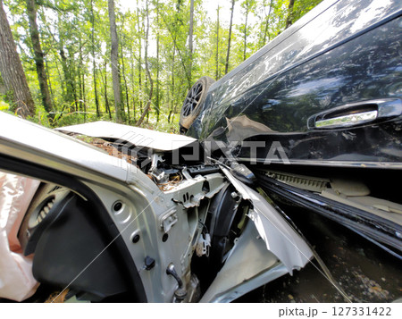 Two cars are involved in serious collision on wooded road, with one vehicle overturned debris scattered around. 127331422