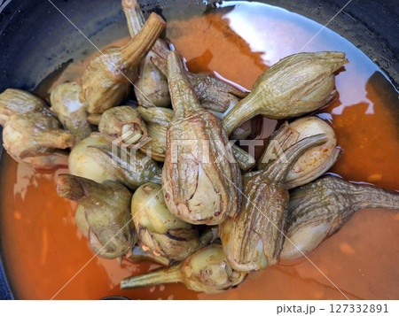 Vibrantly colored pickled eggplant ovaries are displayed in a jar at a bustling farmer's market in Spain, highlighting the region's rich agricultural heritage and culinary traditions. 127332891