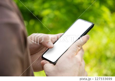 Close up of mans hands holding smartphone in outdoor green setting. Check apps, focused on device, chatting, texting. Fitness progress on app. Side view. Close up. Close up of mans hands holding smartphone in outdoor green setting. Check apps, focused on device, chatting, texting. Fitness progress on app. Side view. Close up. 127333699