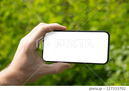 Man hand holding mobile phone with white blank screen against blurred green background. Showcasing mobile apps, design mockups, or digital content presentations. Check apps. Summer heat weather. Man hand holding mobile phone with white blank screen against blurred green background. Showcasing mobile apps, design mockups, or digital content presentations. Check apps. Summer heat weather. 127333702