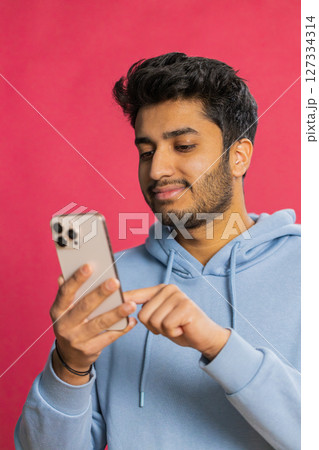 Happy Indian young man browsing social media smiling typing message on smartphone engaging working 127334314