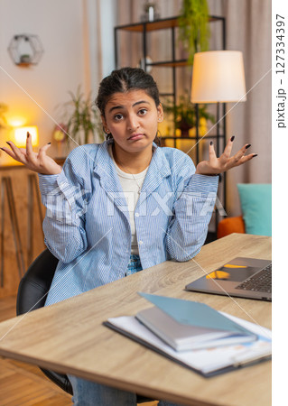 Uncertain young Indian woman freelancer shrugging shoulders don't know how to work at office table 127334397