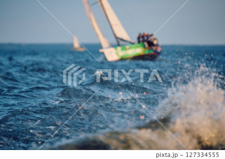 Sailing regatta in the Gulf of Finland at sunset, sailing yacht competing in a race, splashing water from under the boat, teamwork, board the boat Sailing regatta in the Gulf of Finland at sunset, sailing yacht competing in a race, splashing water from under the boat, teamwork, board the boat 127334555