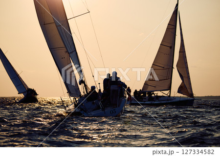 Sailing regatta in the Gulf of Finland at sunset, few sailing yachts competing in a race, splashing water from under the boats, teamwork, board the boat Sailing regatta in the Gulf of Finland at sunset, few sailing yachts competing in a race, splashing water from under the boats, teamwork, board the boat 127334582