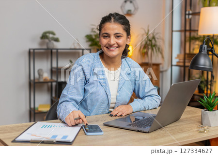 Indian woman working with financial graphs, calculate taxes for charts and reports at desk at home 127334627