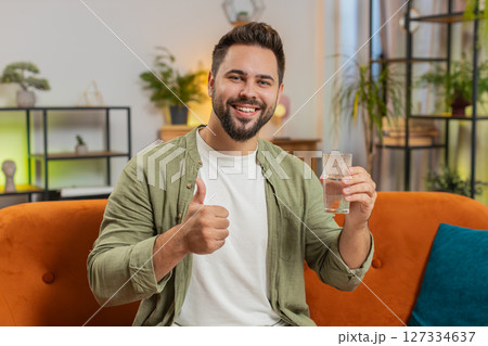 Smiling Caucasian man sitting on sofa leading healthy lifestyle, drinking a glass of pure water 127334637
