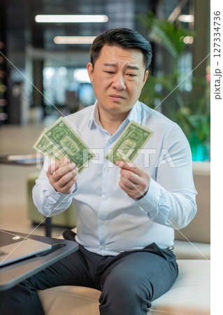 Upset businessman feeling worried about financial problems bad day sitting in modern office lobby Upset businessman feeling worried about financial problems bad day sitting in modern office lobby 127334736
