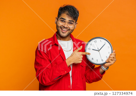 Indian young man showing time hour on wall office clock, ok, thumb up, approve, hurry up, deadline Indian young man showing time hour on wall office clock, ok, thumb up, approve, hurry up, deadline 127334974