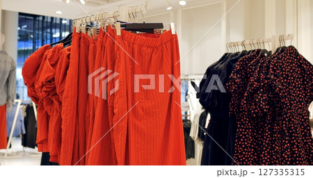 Vibrant red pants and black dresses featuring heart patterns hanging elegantly on clothing racks, creating striking visual merchandising display in retail environment. Concept fashion clothes Vibrant red pants and black dresses featuring heart patterns hanging elegantly on clothing racks, creating striking visual merchandising display in retail environment. Concept fashion clothes 127335315