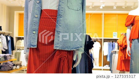 Fashion retail store presenting various clothing items on mannequins, including a stylish denim jacket, white shirt, and a vibrant red skirt combination. Concept fashion clothes 127335317