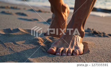 Bare feet treading softly on golden sand, leaving delicate imprints while waves gently caress coastal shoreline during warm sunset moment 127335591