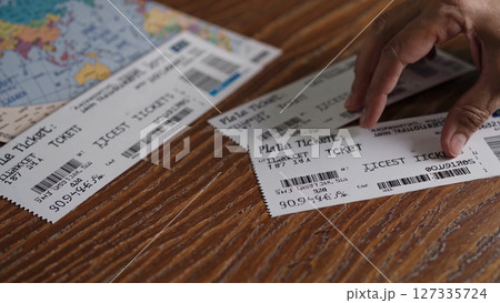 Hand carefully lifting plane ticket from weathered wooden surface, world map backdrop highlighting global travel journey and destination anticipation 127335724