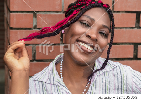 Happy African American Woman Showing Off Colorful Pink and Black Braids Against Brick Wall 127335859