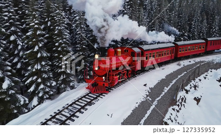 Vintage red locomotive releasing billowing white smoke, traveling across snow laden tracks through dense winter evergreen landscape. concept of steam locomotive in winter forest 127335952