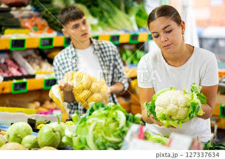 Positive couple choosing foods in fruit and vegetable section of supermarket 127337634