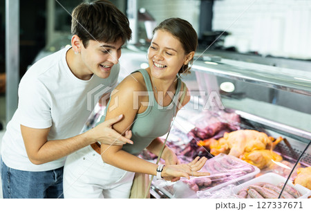 Spouse near butcher shop window inspects goods and choose sausages for grill Spouse near butcher shop window inspects goods and choose sausages for grill 127337671