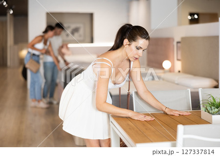 Young woman choosing convenient table in furniture shop Young woman choosing convenient table in furniture shop 127337814