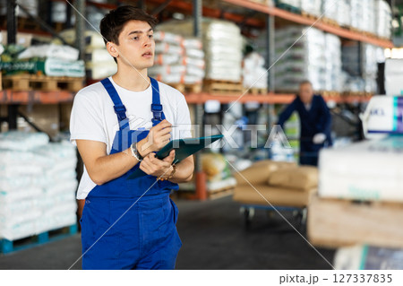 In warehouse of store, guy checks quantity of goods and receipt documents for products 127337835