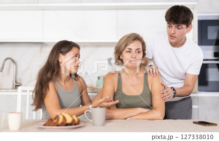 Sad mom sits silently in kitchen, adult children, guy and girl sympathize and comfort woman 127338010