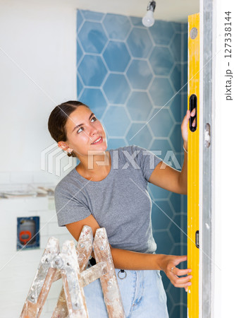 Portrait of a young woman using a spirit level on the bathroom wall 127338144
