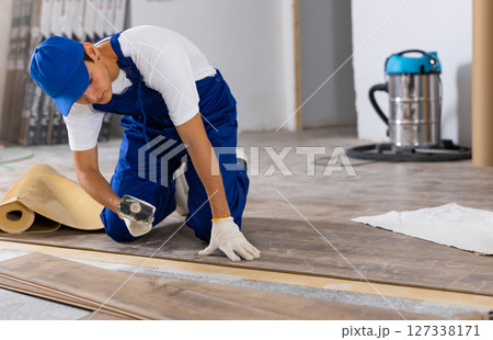 Young builder laying laminate flooring with rubber mallet in repairable room Young builder laying laminate flooring with rubber mallet in repairable room 127338171