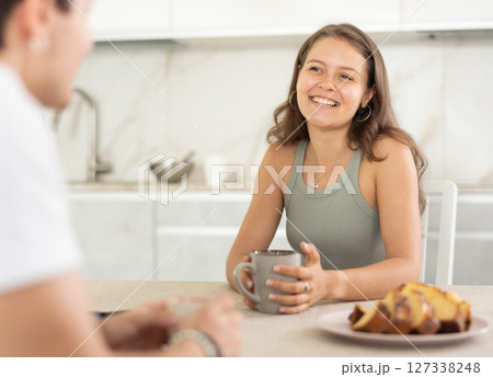 Happy young couple sitting at the kitchen-table and having conversation while drinking tea Happy young couple sitting at the kitchen-table and having conversation while drinking tea 127338248