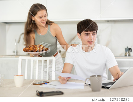 Young woman offering pie to guy working at laptop 127338283
