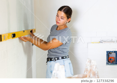 Portrait of a young woman using a spirit level on the bathroom wall 127338296