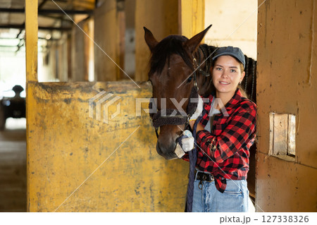 Portrait of smiling woman horse farm worker standing at stable 127338326