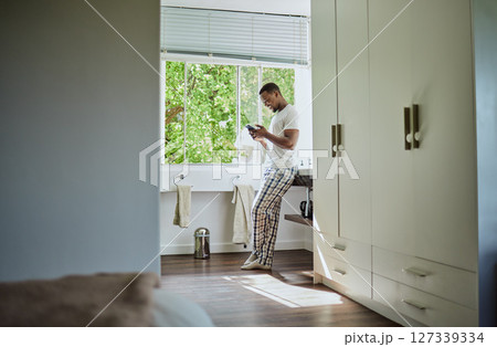 Phone, bathroom and black man in home on social media, texting or internet browsing. Relax, cellphone or happy male holding mobile smartphone for web scrolling, networking or messaging alone in house 127339334