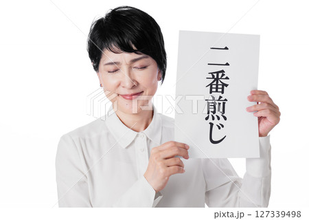 二番煎じと書かれた紙を両手で持ち目を伏せ微笑む中年女性 127339498