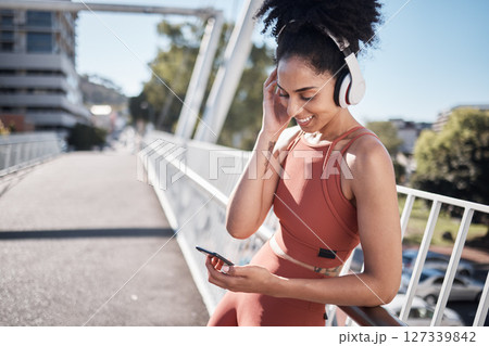 Music headphones, fitness and black woman with phone for social media in city. Exercise, sports and female athlete streaming radio or podcast on 5g mobile smartphone after training outdoors on street Music headphones, fitness and black woman with phone for social media in city. Exercise, sports and female athlete streaming radio or podcast on 5g mobile smartphone after training outdoors on street 127339842