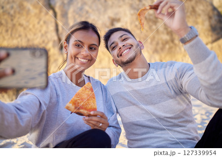 Happy couple, selfie and pizza while at the beach for a picnic date together with food, phone and happiness outdoor in nature. Man and woman with smartphone and lunch while online for profile update 127339954