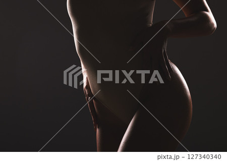 Beauty, body and silhouette of a woman in studio with a sensual, seductive and natural pose. Wellness, body care and shadow figure of a slim girl model posing while isolated by dark black background. 127340340