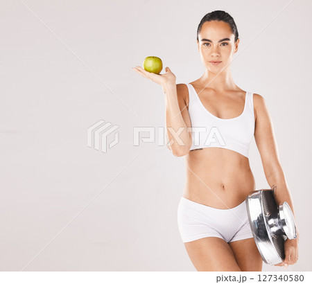 Fitness, health and woman with scale and apple for weightloss, diet and nutrition on white background. Exercise, wellness and girl with fruit, slim body and weight measurement for healthy lifestyle 127340580