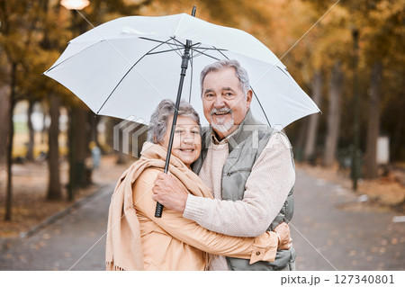 Winter, hug and senior couple in a park, retirement date and walking in Canada with an umbrella. Nature affection, smile and portrait of an elderly man and woman on a walk for happiness and love 127340801