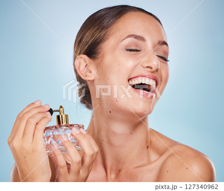 Perfume, product and fragrance with a model woman spraying a scent in studio on a blue background. Spray bottle, luxury and cosmetics with an attractive young female getting ready in the bathroom 127340962