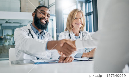 Handshake, partnership or happy doctors in a meeting after successful medical surgery or reaching healthcare goals. Teamwork, woman or black man smiles shaking hands with a worker in hospital office 127340969